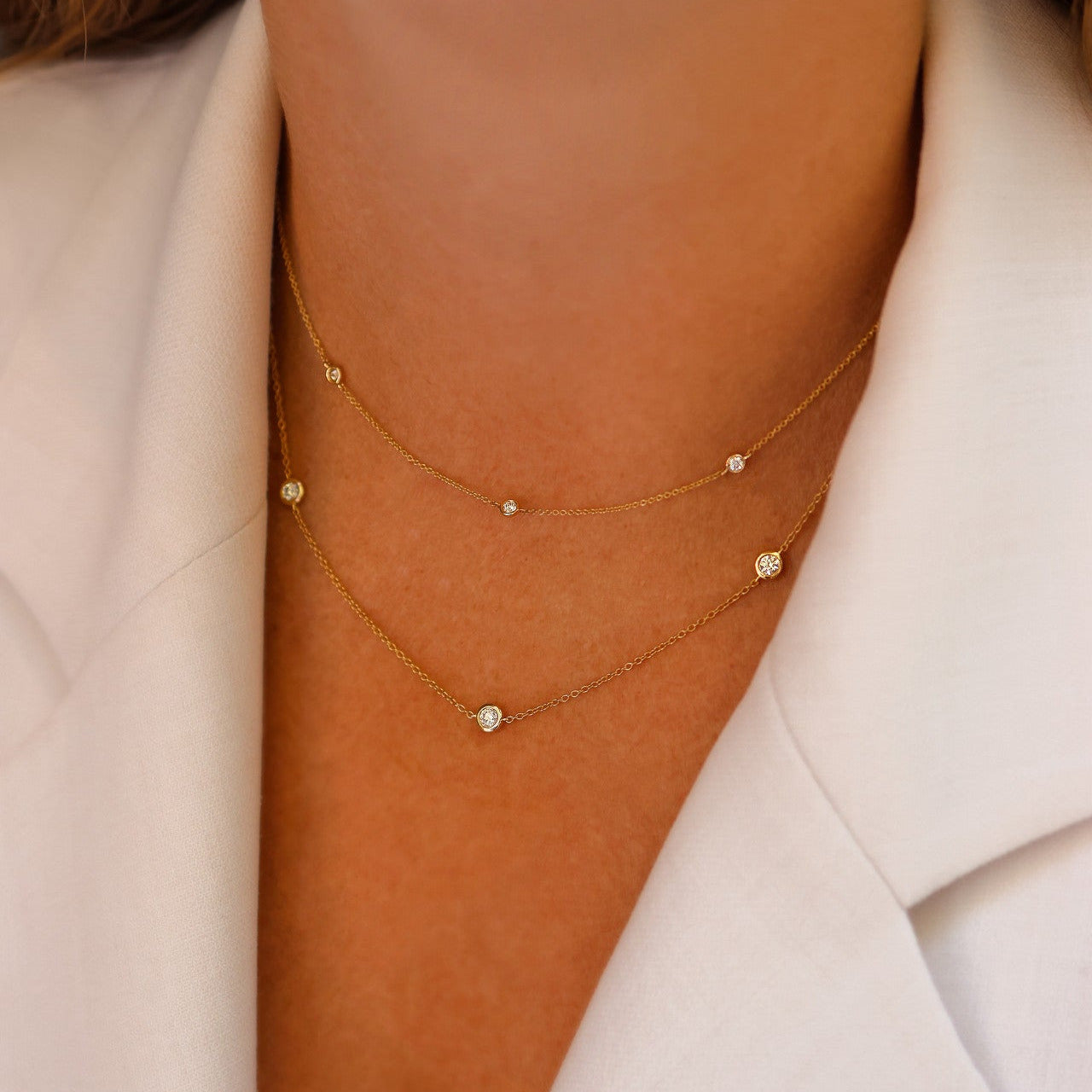 Close-up of a person wearing a delicate gold necklace with small bezel set diamonds